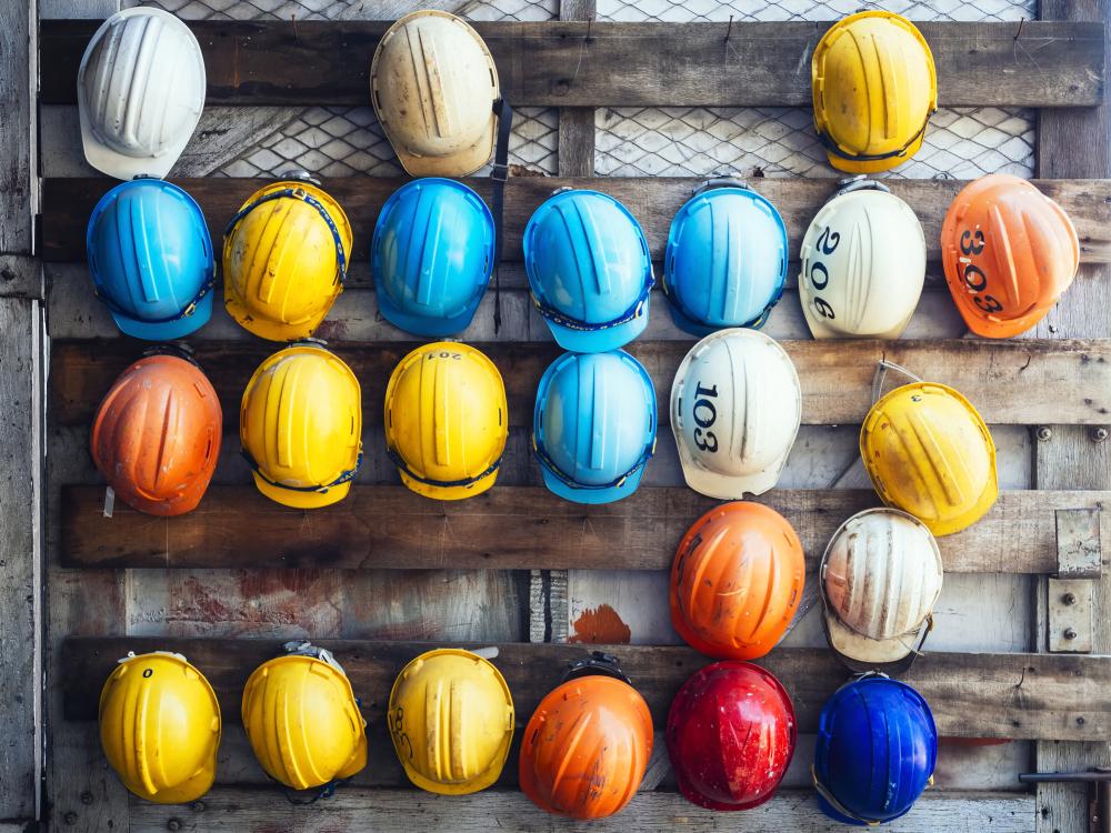 Rows of colorful construction hard hats hung on a wooden wall.