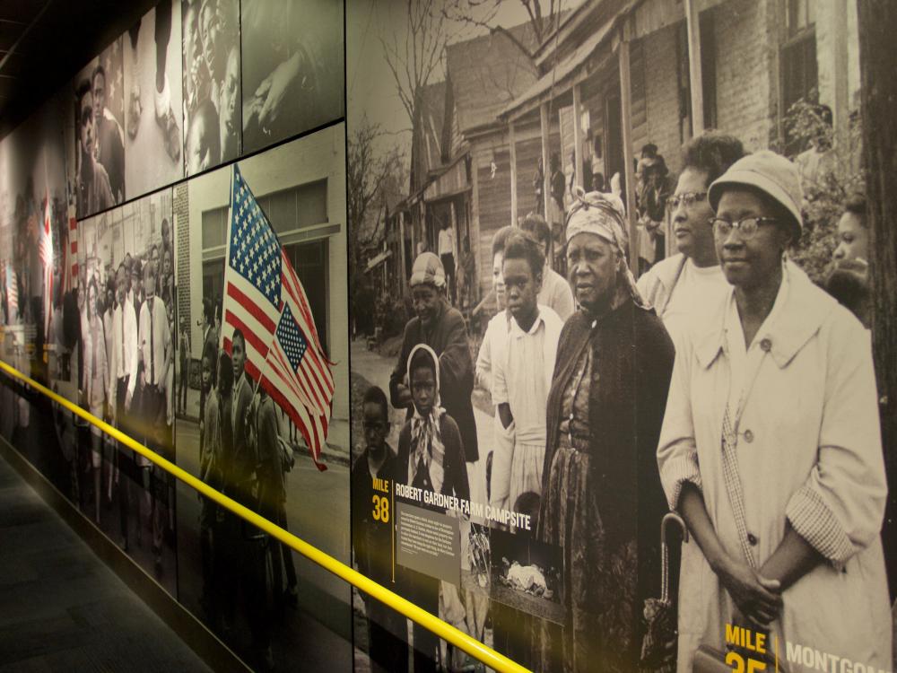 A museum wall display featuring large black-and-white historic photos of African American individuals and civil rights scenes, including people holding an American flag.