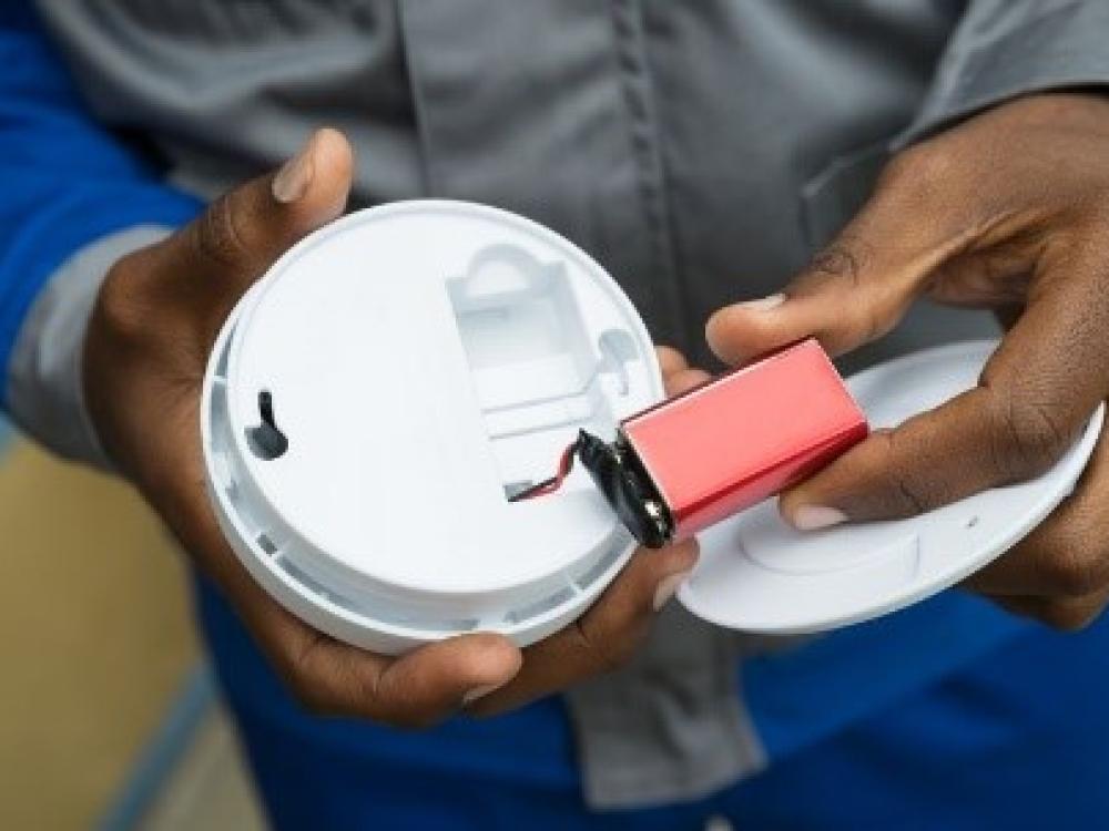 Hands inserting a new battery into a carbon monoxide detector.