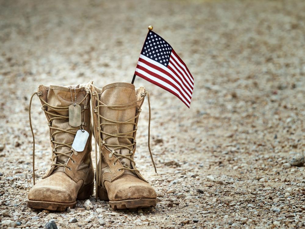 Pair of military combat boots on gravel with dog tags and a small American flag placed between them.