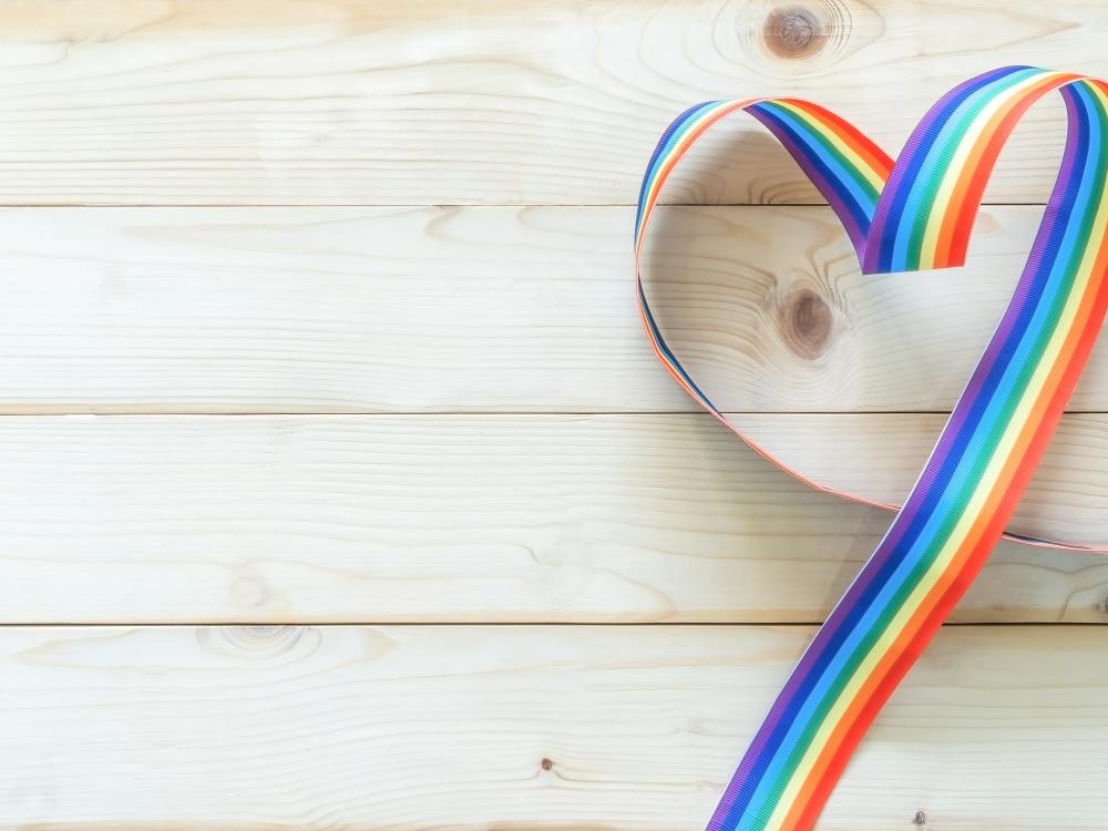 A rainbow-colored ribbon shaped into a heart on a light wooden background.