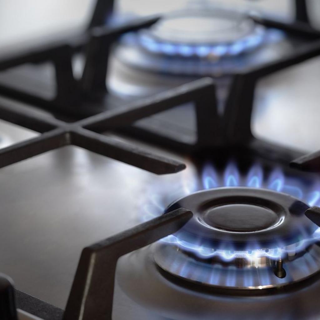 Close-up of a gas stove with blue flames burning on multiple burners beneath black metal grates.
