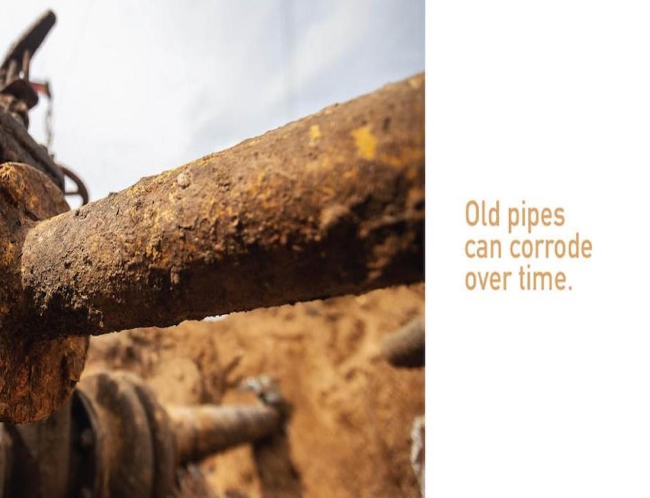 Close-up of an old, rusted metal pipe partially buried in the ground, illustrating pipeline corrosion over time.