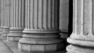 Black-and-white close-up of large stone columns lining the exterior of a classical government building.
