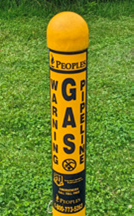 Yellow gas pipeline warning marker post labeled ‘Gas’ standing in grass.