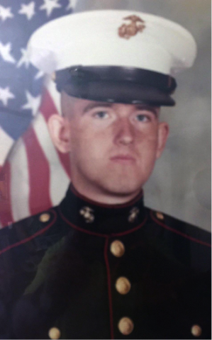 Rickie Daniels, a U.S. Marine in dress uniform poses for a formal portrait with an American flag in the background.