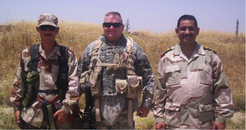 A group of three veterans standing in a field. John Aulbach is in the center 