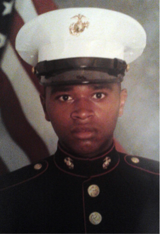Kirklyn Fields A U.S. Marine in dress uniform poses for a formal portrait with an American flag in the background.