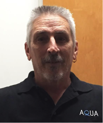Roger Tupps wearing a black polo shirt with an Aqua logo stands indoors and looks toward the camera.