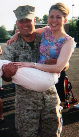 Service member, Lawrence Weaver in camouflage uniform smiles while holding a woman in his arms outdoors.